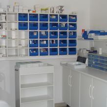 Cuarto de almacenamiento blanco con contenedores y estantes azules, armarios y un fregadero para organizar los suministros.