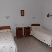 Habitación sencilla con dos camas individuales, mesitas de noche de madera y paredes blancas.