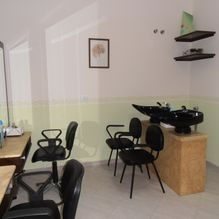 Pequeña sala de espera con sillas negras, un armario de madera, estantes en la pared y un cuadro enmarcado en una pared clara.