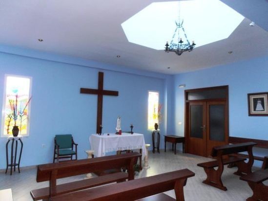 Pequeña capilla con bancos de madera, una gran cruz y vidrieras.