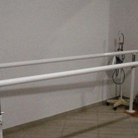 Dos barras de soporte paralelas blancas en una habitación clínica junto a una pared y un suelo de color beige.