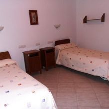 Habitación pequeña con dos camas individuales, mesitas de noche y paredes blancas.