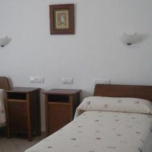 Habitación de hotel pequeña con una cama individual, dos mesitas de noche, lámparas de pared y cuadros enmarcados.
