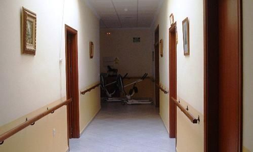 Largo pasillo con paredes beige y pasamanos de madera, que conduce a los aparatos de ejercicio al final del pasillo.