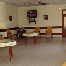 Sala de recreo vacía con sillas, mesas pequeñas y un televisor montado en la pared.