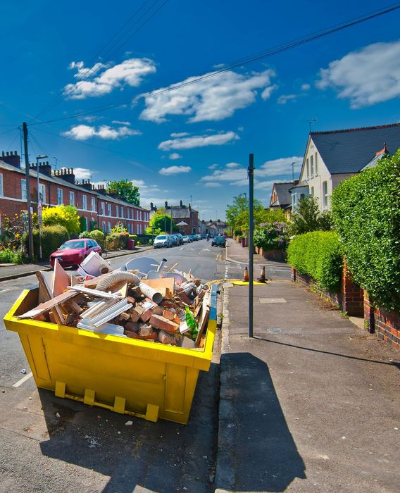 Benne jaune remplie de déchets devant une maison