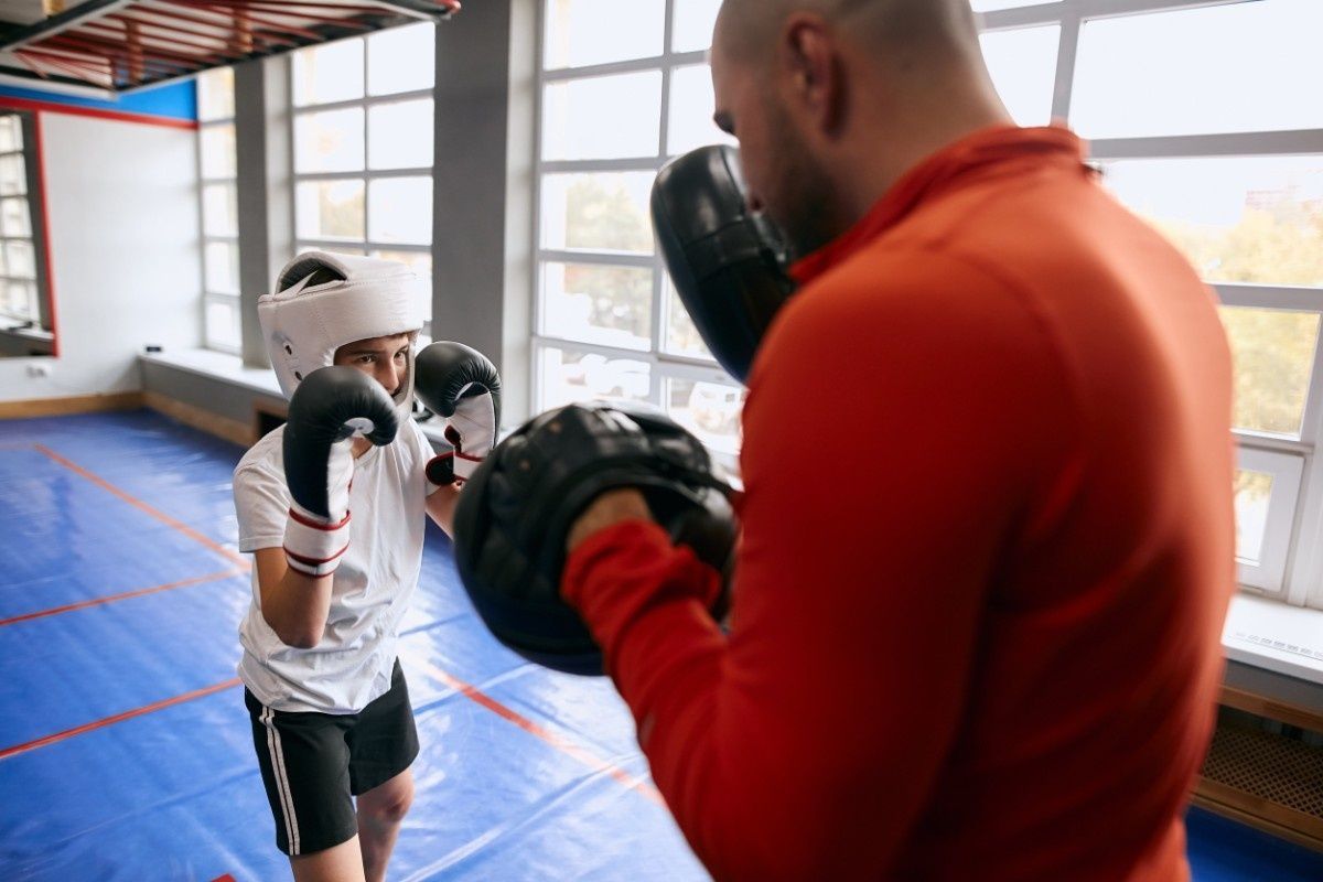 Persona joven boxeando con entrenador en el gimnasio.