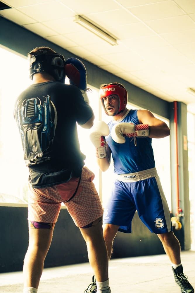 Persona joven boxeando con entrenador en el gimnasio.