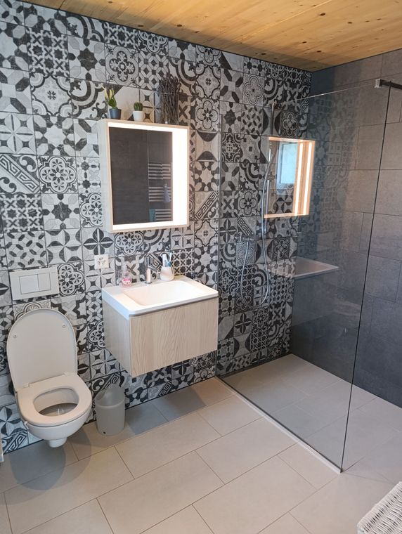 Salle de bain avec mur d'accent en carrelage à motifs, vanité flottante, toilettes et cabine de douche en verre.