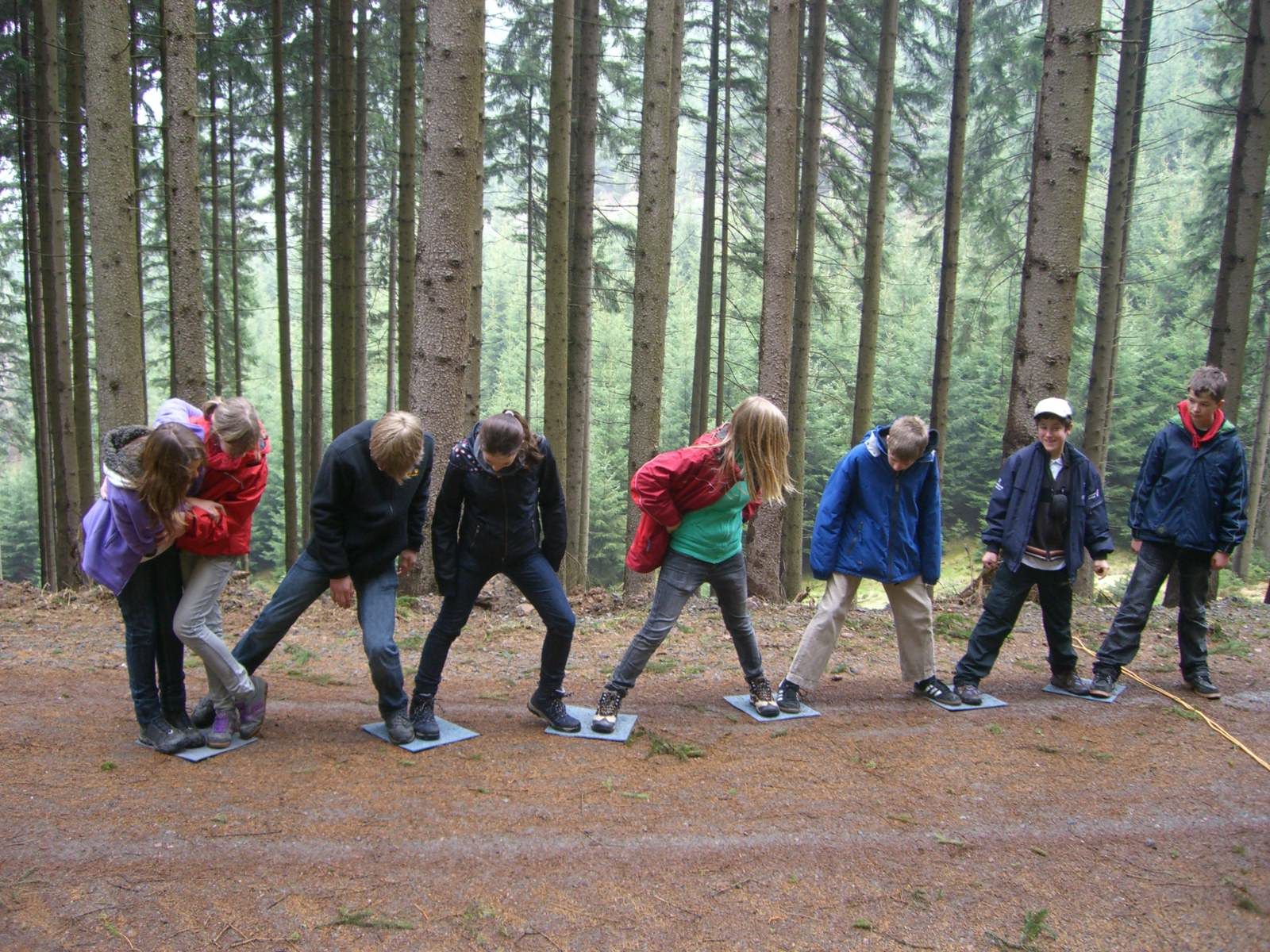 Kinder spielen im Freien ein Mannschaftsspiel und stehen auf quadratischen Plattformen in einem Wald.
