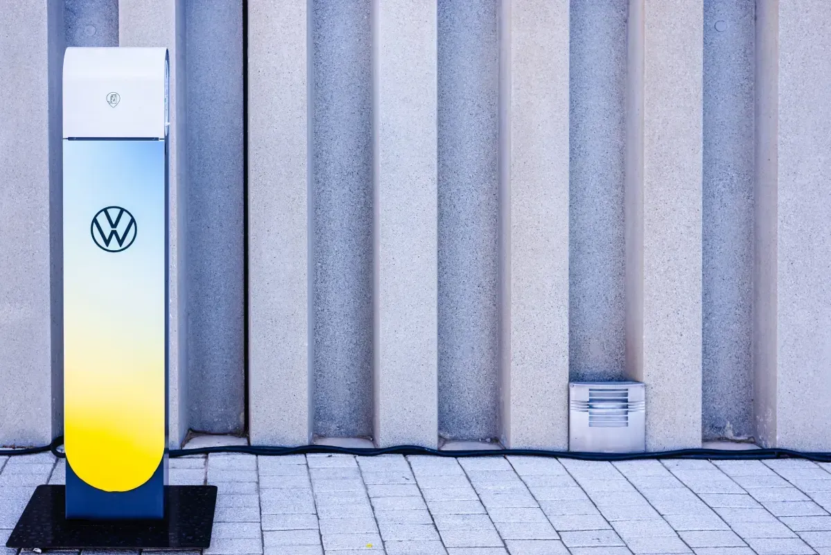 Estación de carga de VW junto a una pared ondulada, con una base que degrada el color amarillo al azul