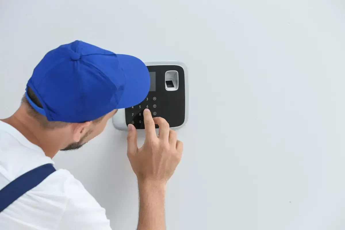 Técnico con gorro azul ajustando el teclado de un sistema de seguridad montado en la pared.
