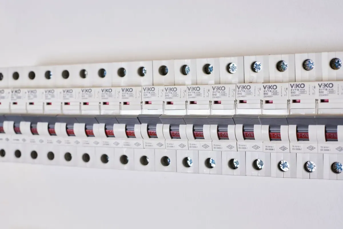 Panel de control eléctrico con filas de disyuntores y cables de colores dentro de un gabinete.