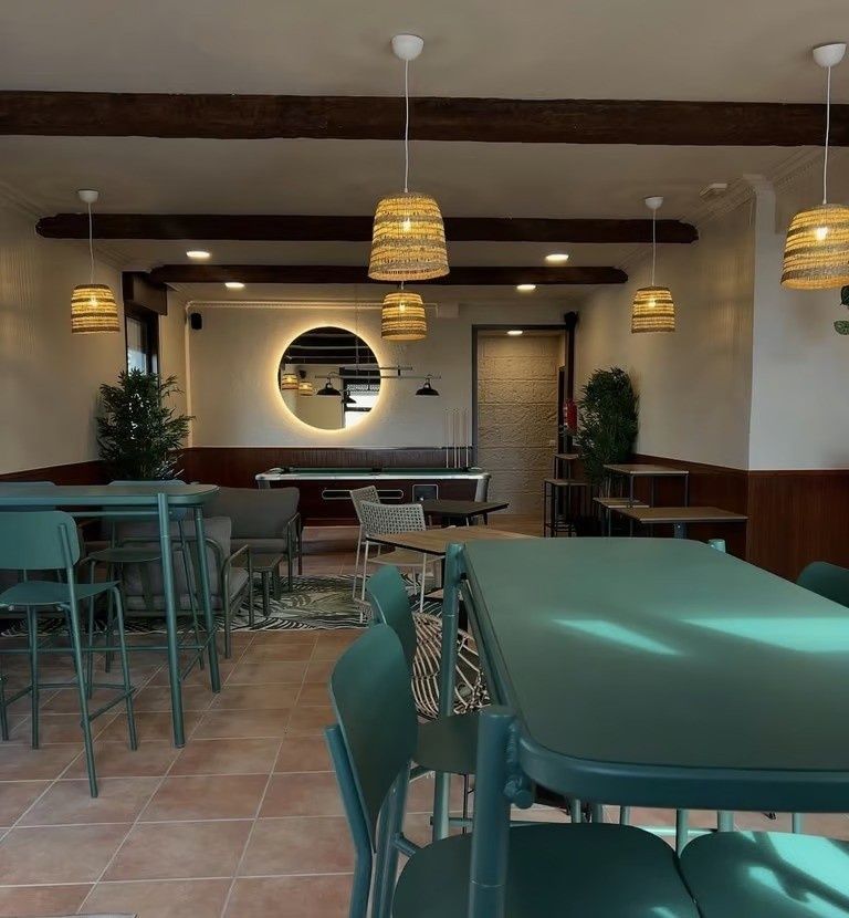 Interior de cafetería moderna y vacía con sillas y mesas de color verde azulado, lámparas colgantes tejidas
