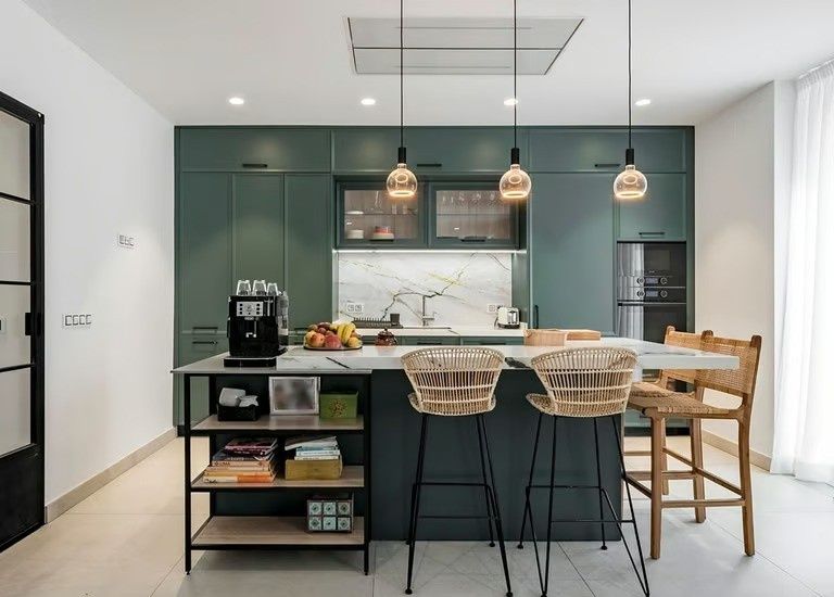 Cocina moderna con isla, tres lámparas colgantes, taburetes de bar y cafetera en la encimera.