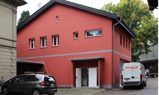 Ein rotes Gebäude mit einem davor geparkten weissen Lieferwagen. Foto von witschi malerei.