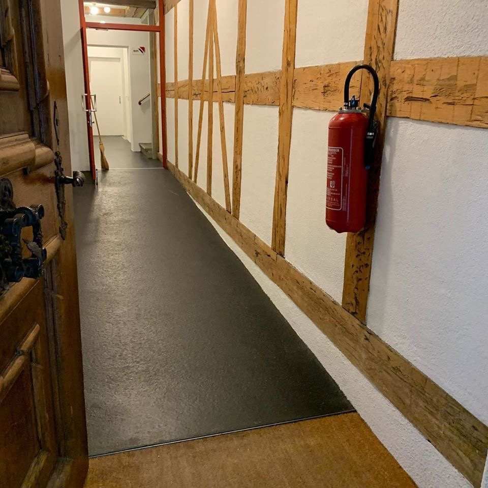 Ein roter Feuerlöscher hängt an einer Wand in einem Flur. Foto von der Witschi Malerei.
