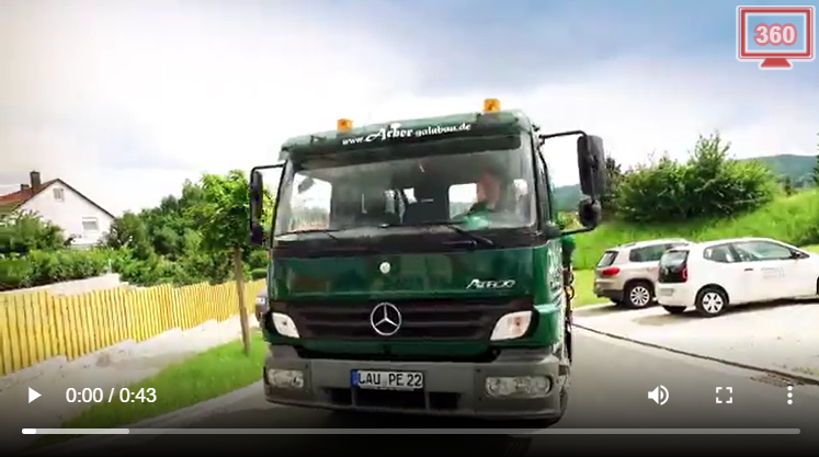 Ein grüner Mercedes-Benz-Lkw mit dem Kennzeichen LAU PE 22 fährt auf einer Straße in der Nähe einer Grünfläche mit geparkten Autos.