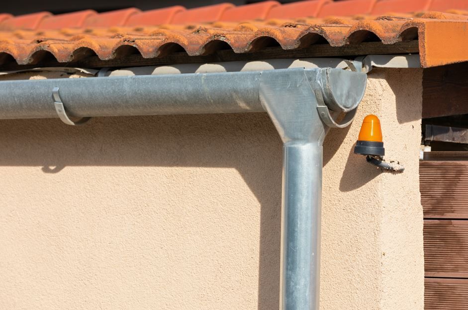 Sistema de canalones con bajante y luz de advertencia naranja fijado a una pared de color claro.