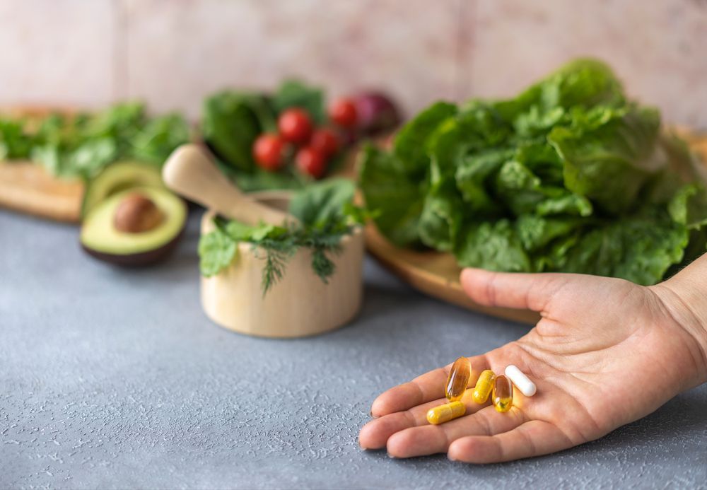 Una persona sostiene una pastilla en su mano delante de verduras.