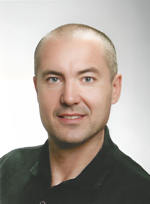 Porträt einer lächelnden Person in einem dunklen Hemd vor hellem Hintergrund