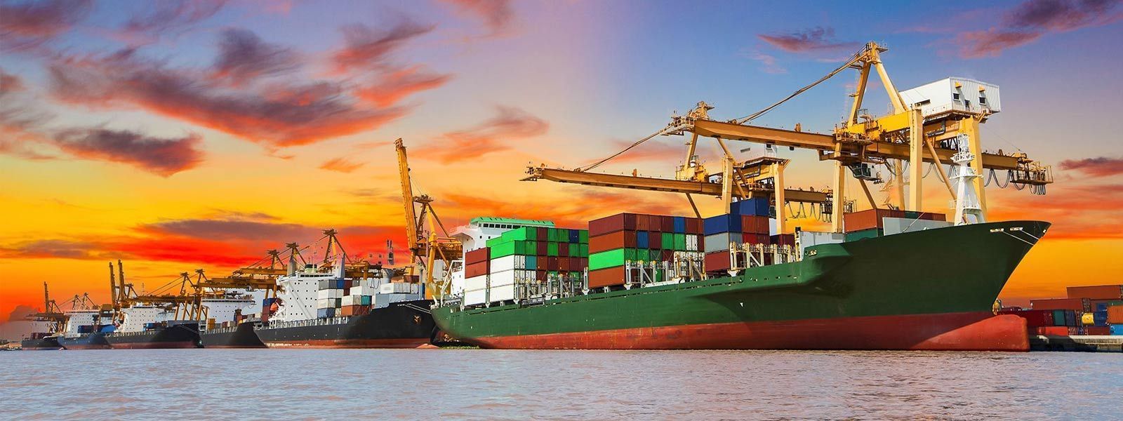 Buque de carga en un puerto, con cielo colorido al atardecer, grúas cargando contenedores.
