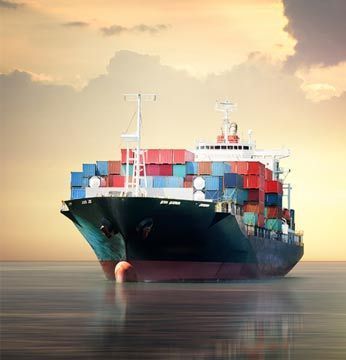 Buque de carga en el océano, cargado con coloridos contenedores de envío, bajo un atardecer nublado.