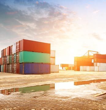 Contenedores de envío apilados en un puerto; cielo brillante.