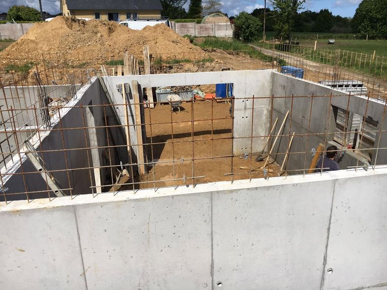 Chantier de construction avec murs de fondation en béton, armatures en acier et monticules de terre en arrière-plan