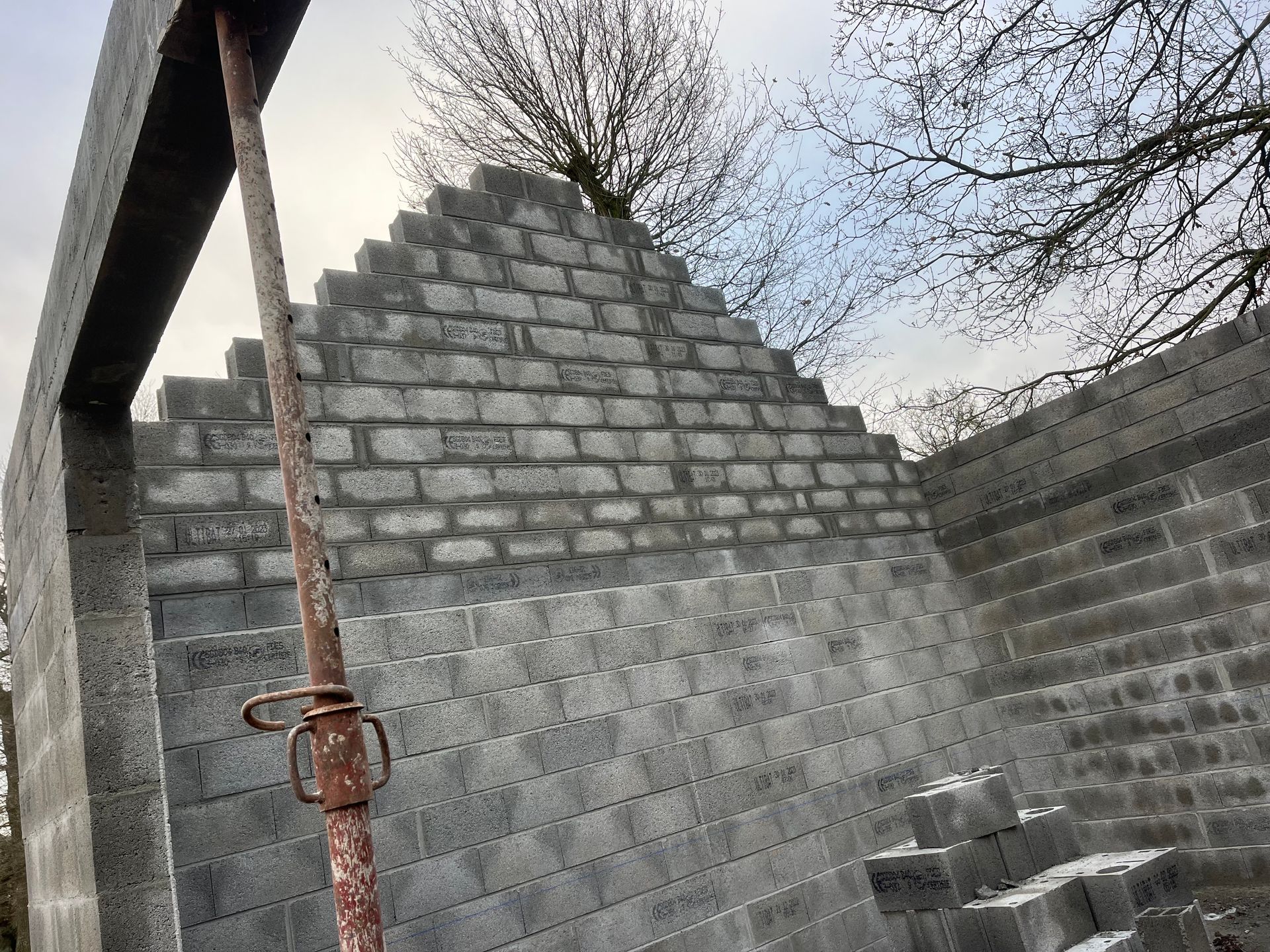 Mur en briques partiellement construit avec un poteau métallique et des marches, à l'extérieur sous des arbres dénudés