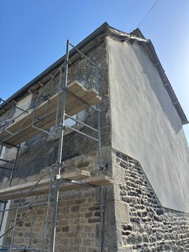 Échafaudages sur un bâtiment en pierre en cours de réparation, avec un mur enduit de plâtre blanc et un ciel bleu.