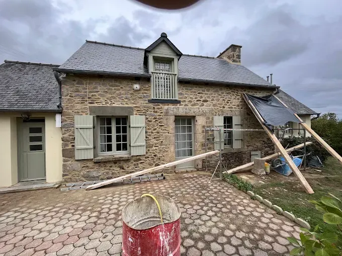 Maison en pierre en rénovation : échafaudages, échelle et matériaux de construction dans l’allée.