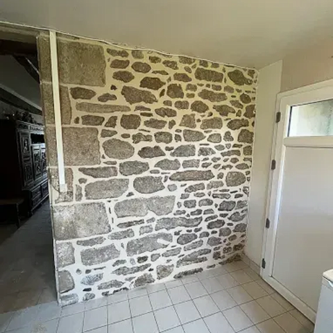 Mur en pierre dans une entrée carrelée, à côté d'une porte blanche et d'une ouverture.
