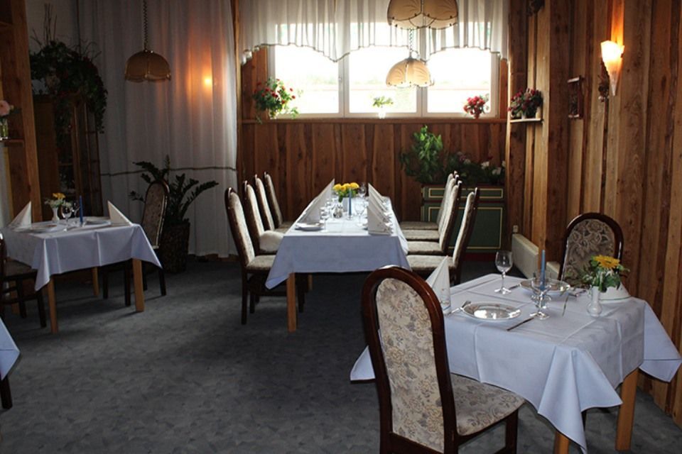 Restaurant-Innenraum mit Holzvertäfelung, mit weißer Tischwäsche gedeckten Tischen und Stühlen.