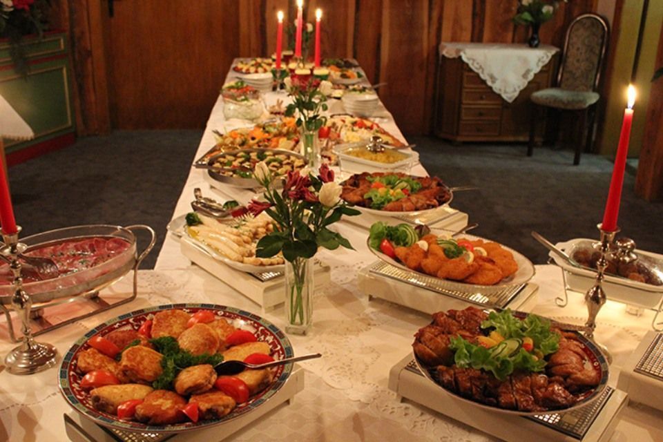 Buffettisch mit verschiedenen Gerichten, beleuchtet von Kerzen. Weiße Tischdecke, Holzvertäfelung im Hintergrund.