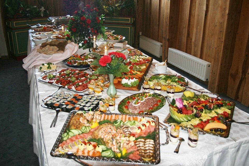 Buffettisch mit einer Vielzahl von Speisen, darunter Sushi, Salate und Wurstwaren, in einem holzgetäfelten Raum.