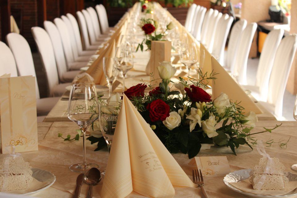 Langer Tisch für den Hochzeitsempfang mit cremefarbener Tischwäsche, Blumengestecken und gefalteten Servietten.