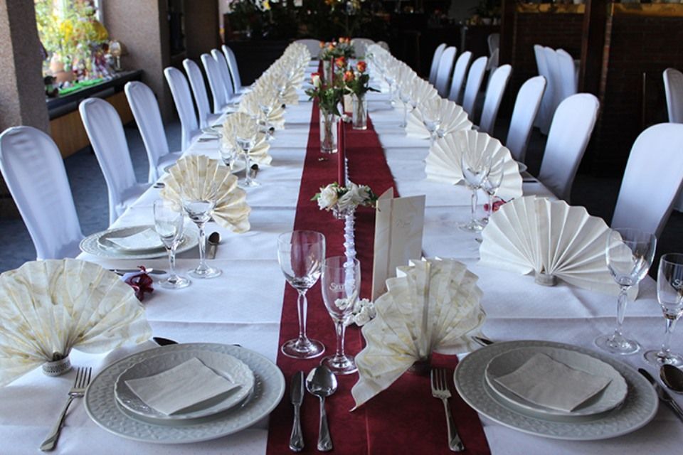 Langer Tisch für eine formelle Veranstaltung mit weißer Tischdecke, rotem Tischläufer und dekorativ gefalteten Servietten.