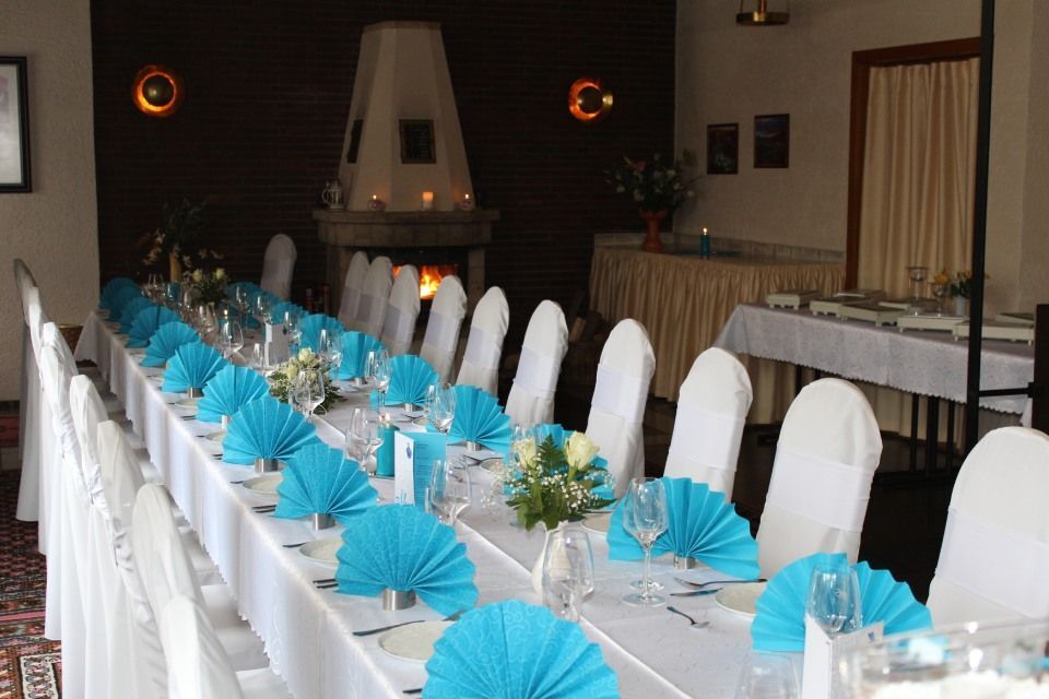 Langer Banketttisch, gedeckt für eine Veranstaltung, mit weißer Tischdecke, türkisfarbenen Servietten und weißen Stuhlhussen.