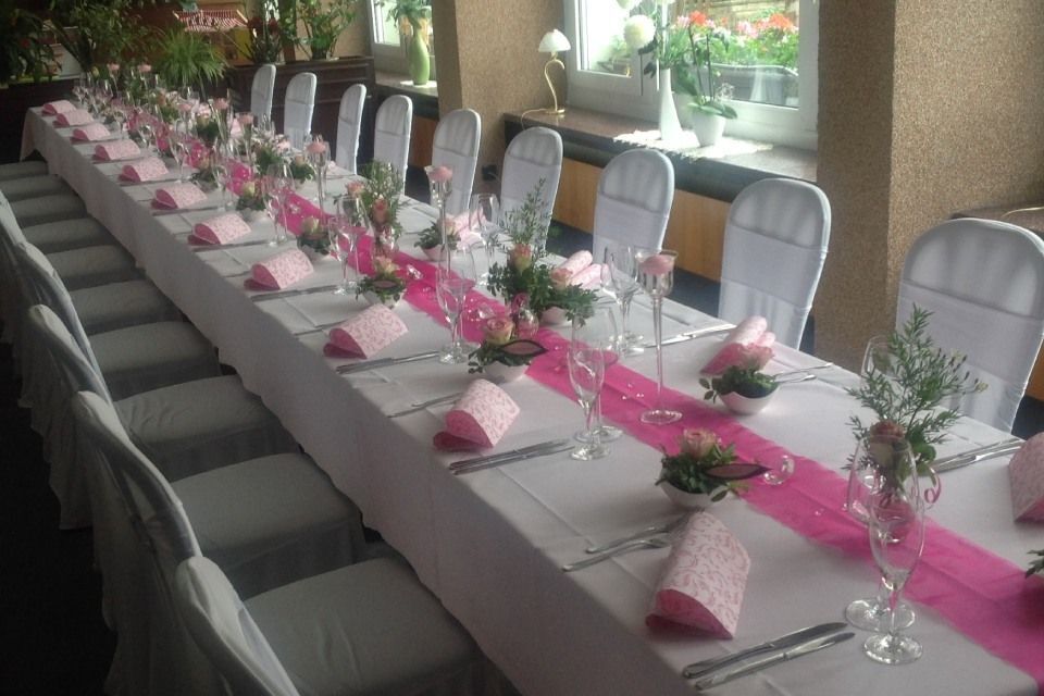 Langer, dekorierter Tisch für eine Feier mit rosa Akzenten und weißen Stuhlhussen.