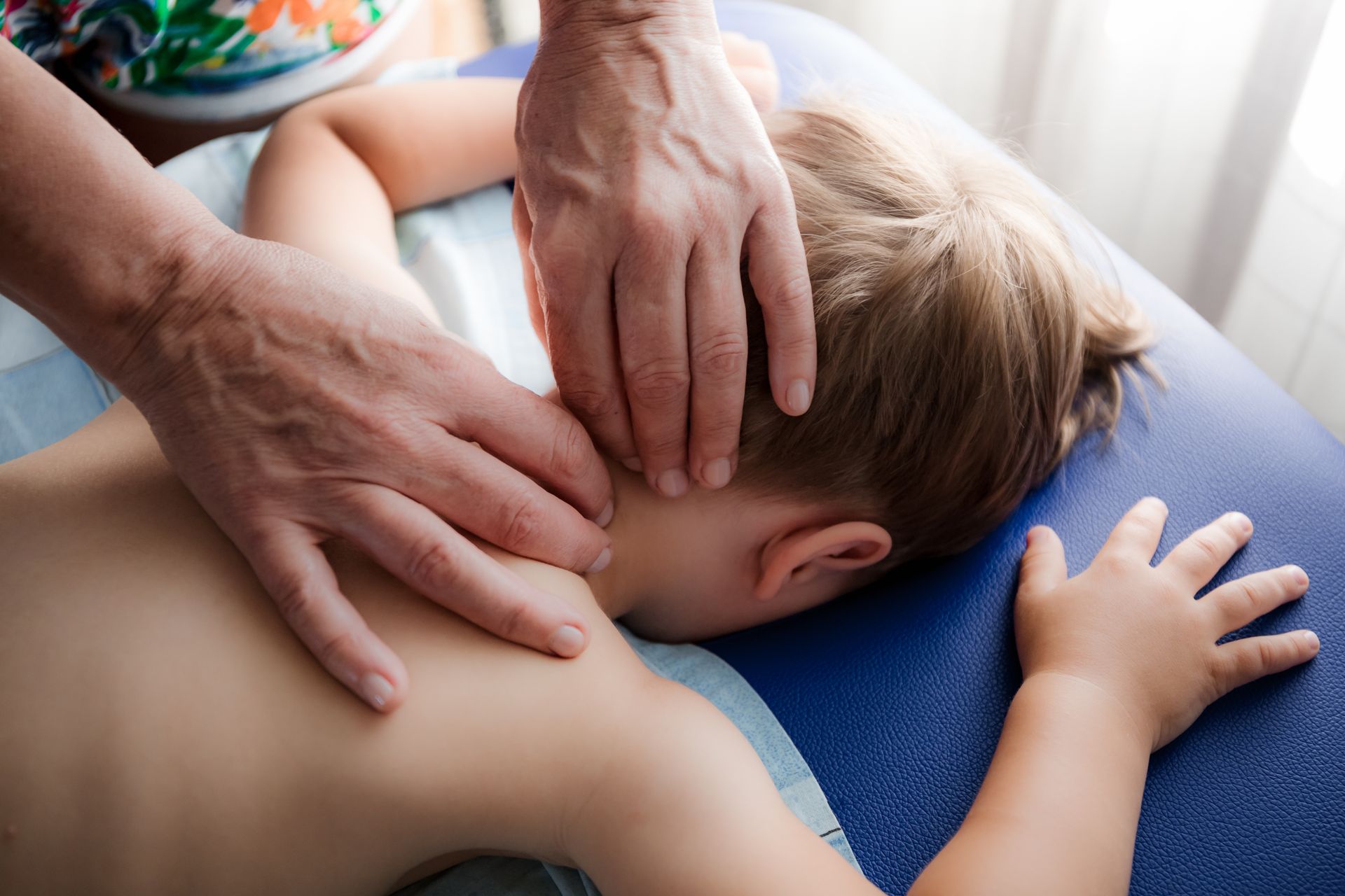 Une personne effectue un massage du dos et du cou à un enfant sur une table de massage bleue.
