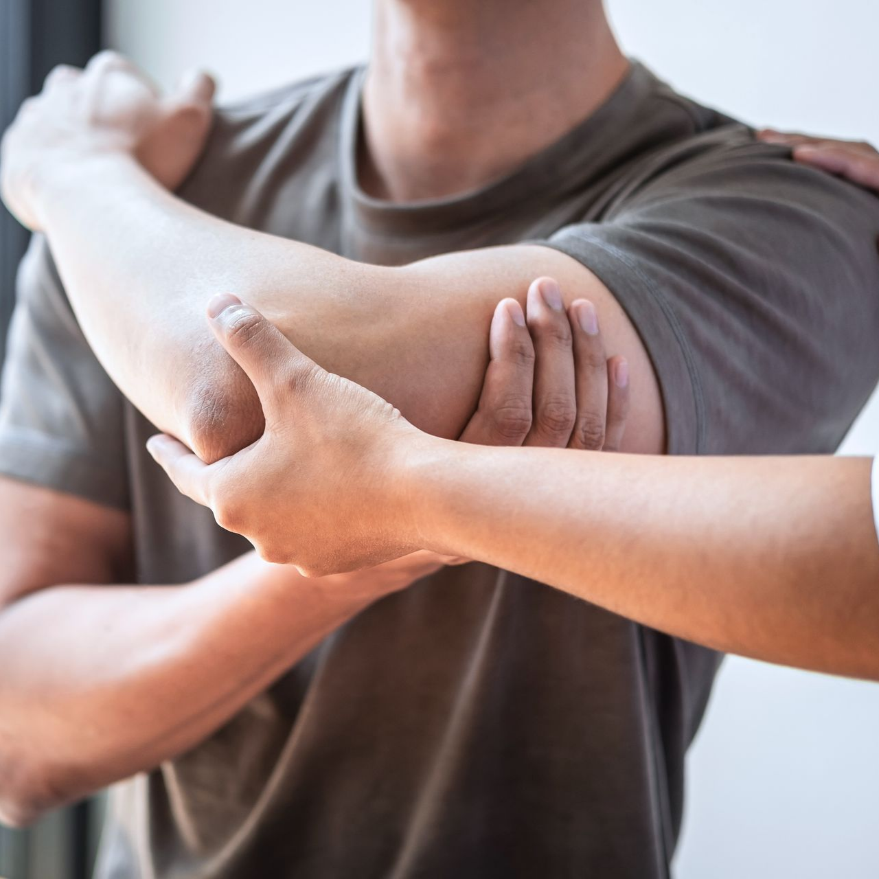 Le bras d'une personne est examiné par un physiothérapeute ; le coude est plié, les mains touchent l'articulation.