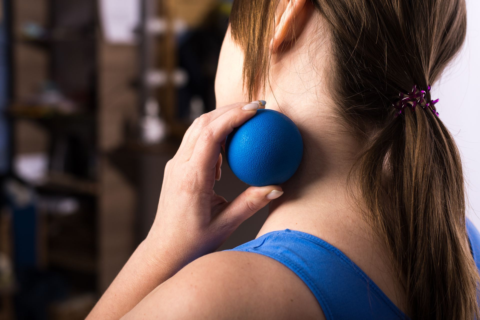 Une femme utilise une balle bleue pour se masser la nuque.