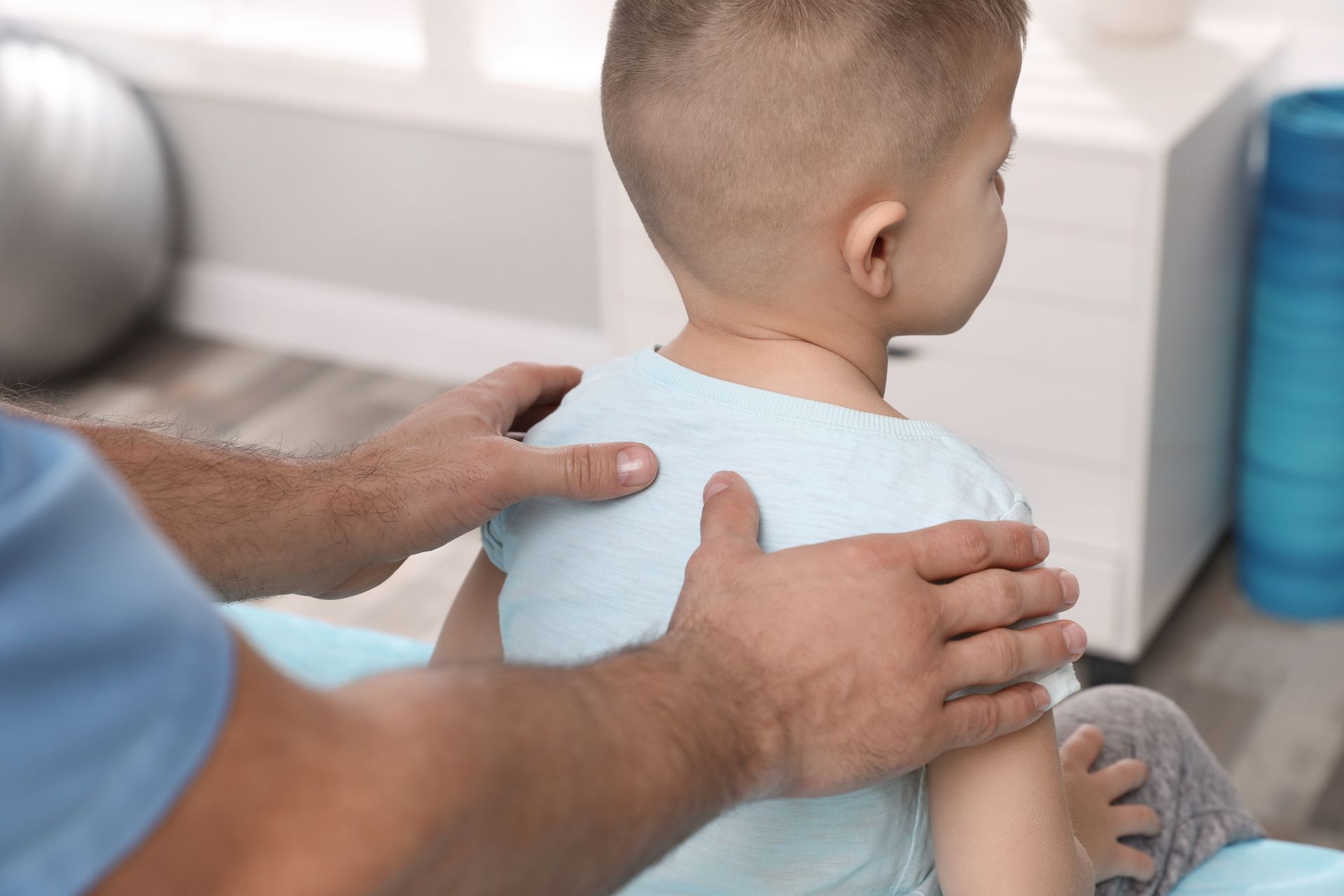 Les mains d'un homme sur les épaules d'un jeune enfant, lors d'une séance de thérapie dans une salle avec des équipements de sport.