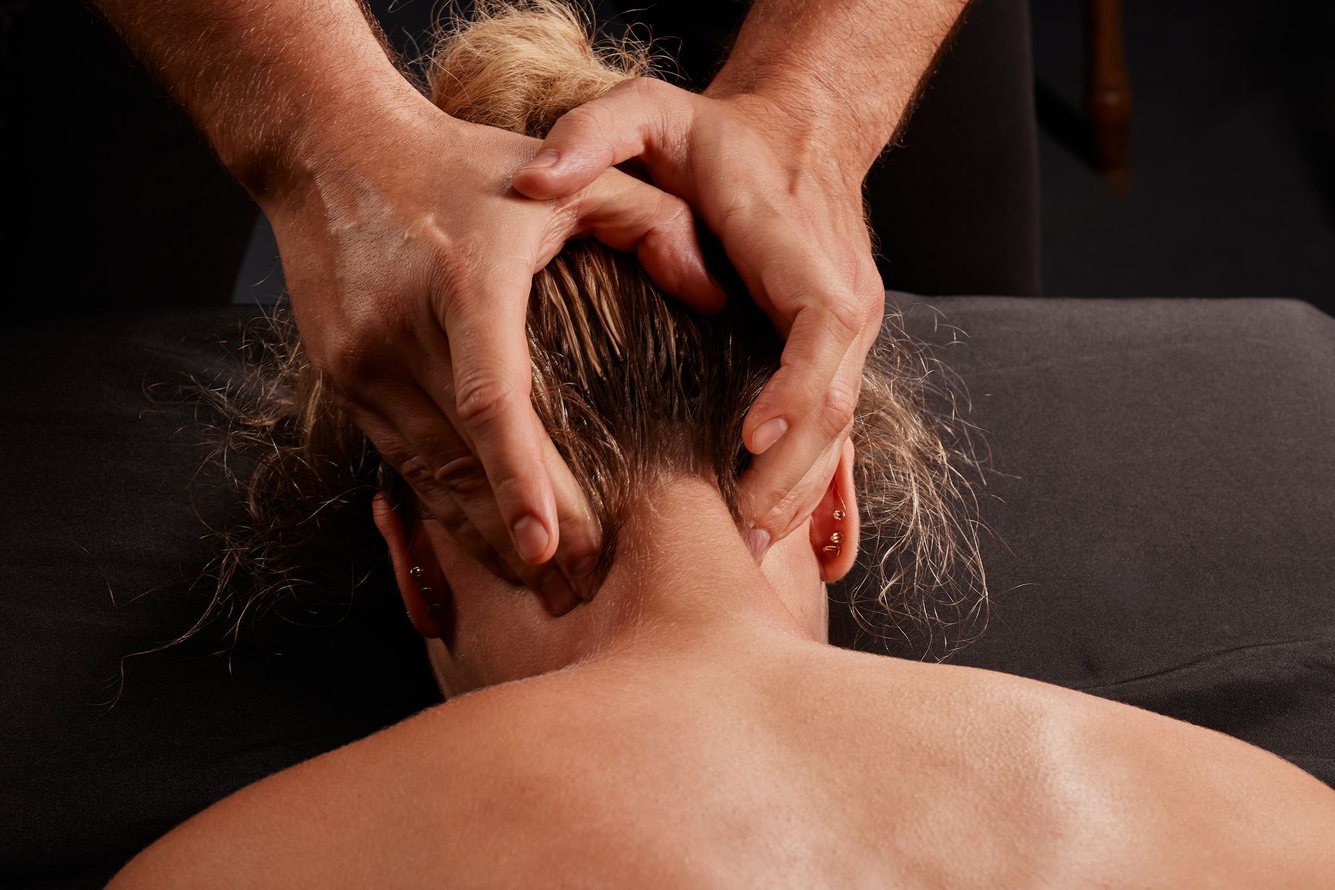 Personne recevant un massage du cou. Les mains sont posées sur la nuque et la tête, dans un environnement sombre.