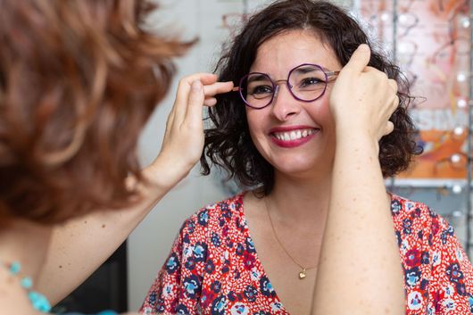 Femme souriante ajustant les lunettes d'une cliente vêtue d'un haut rouge à fleurs.