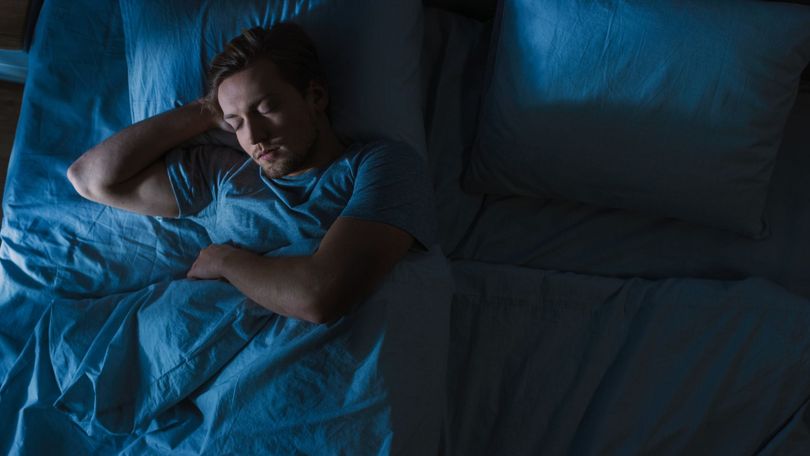 Personne dormant dans un lit sous des draps bleus dans une chambre faiblement éclairée