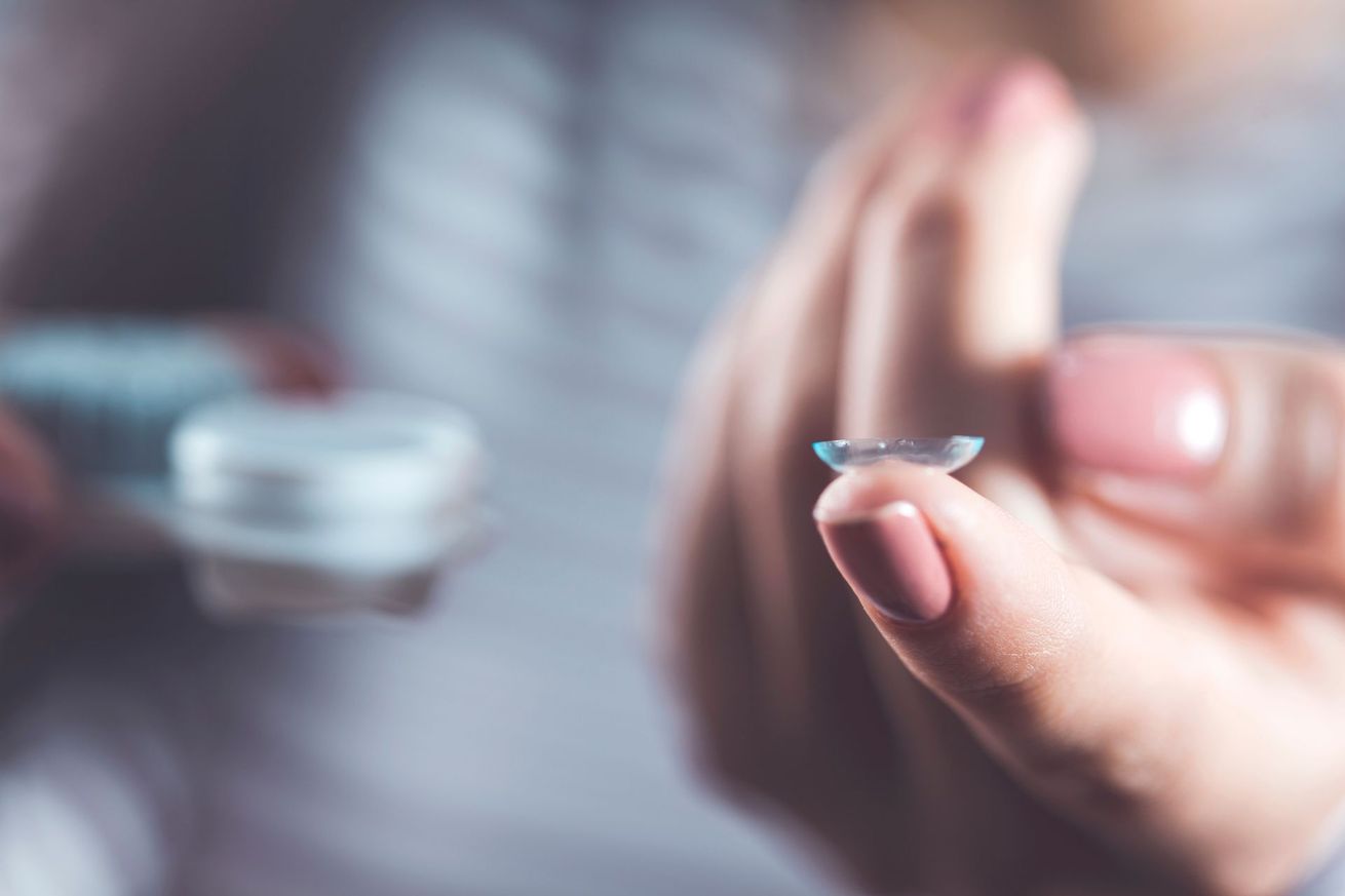 Main tenant une lentille de contact près d'un étui à lentilles flou posé sur une table