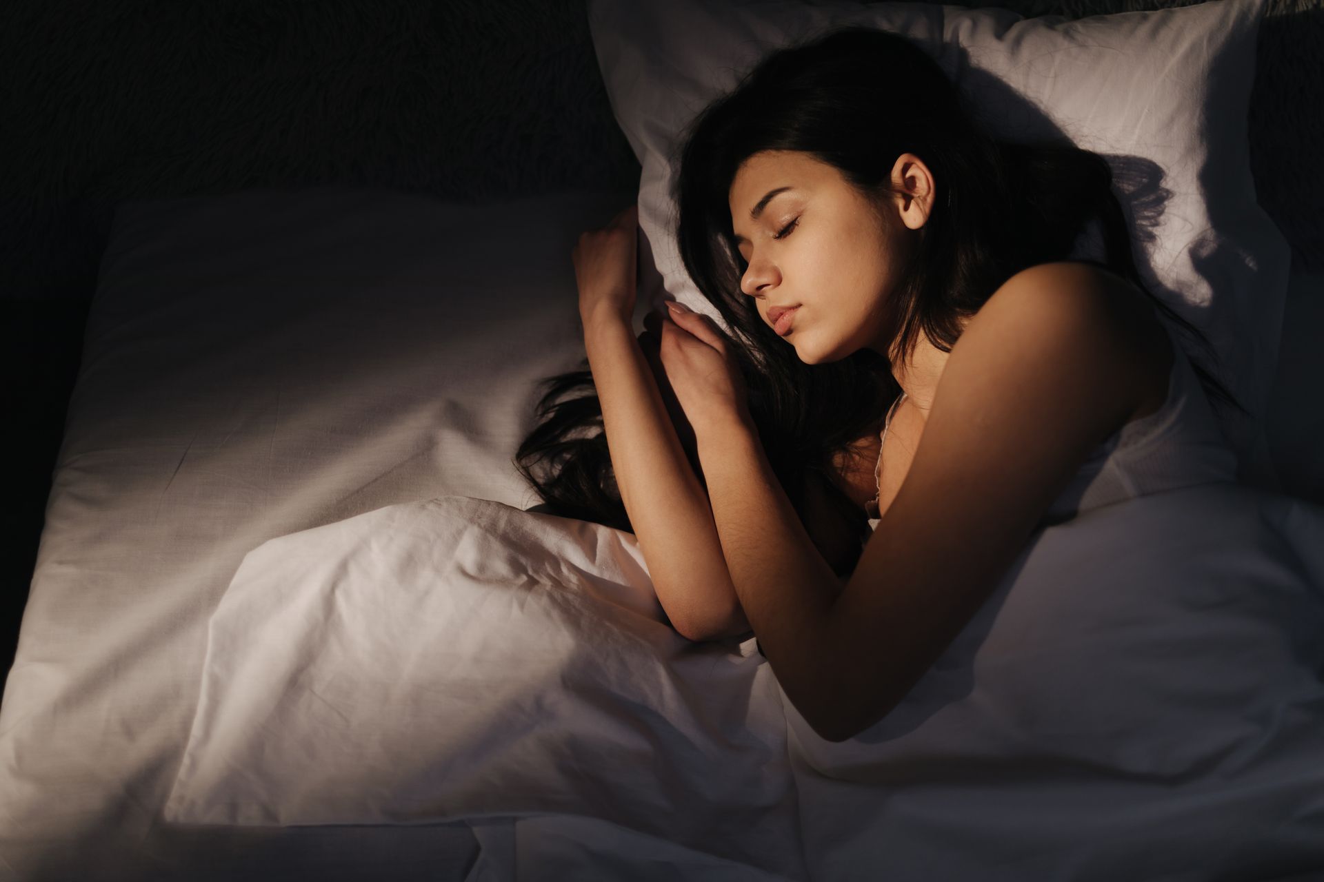 Personne endormie dans son lit, recroquevillée sous des draps blancs sous une lumière tamisée et chaude.