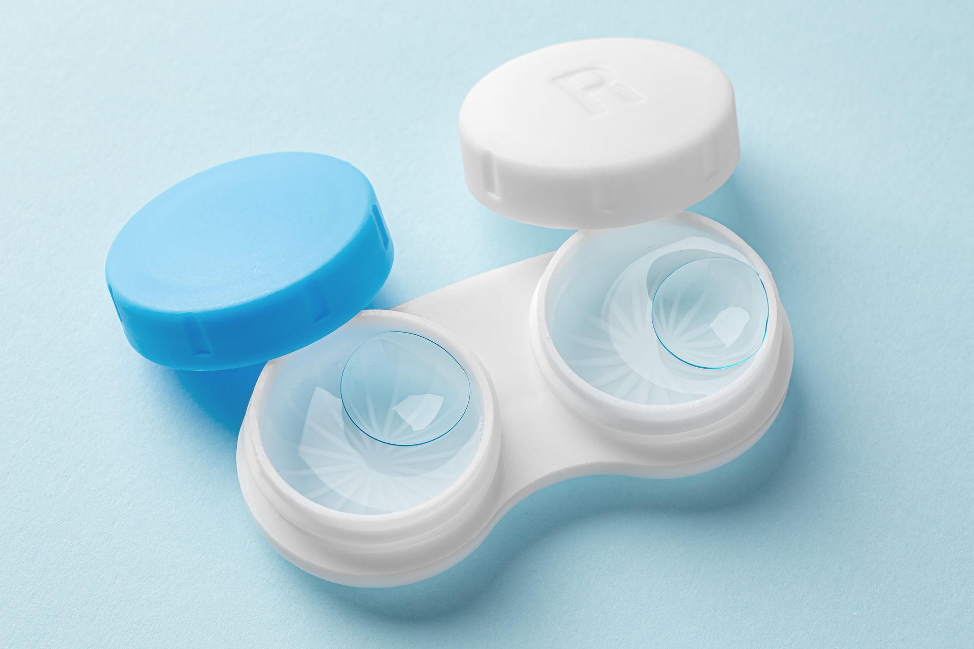 Étui à lentilles de contact bleu et blanc avec lentilles sur fond bleu clair